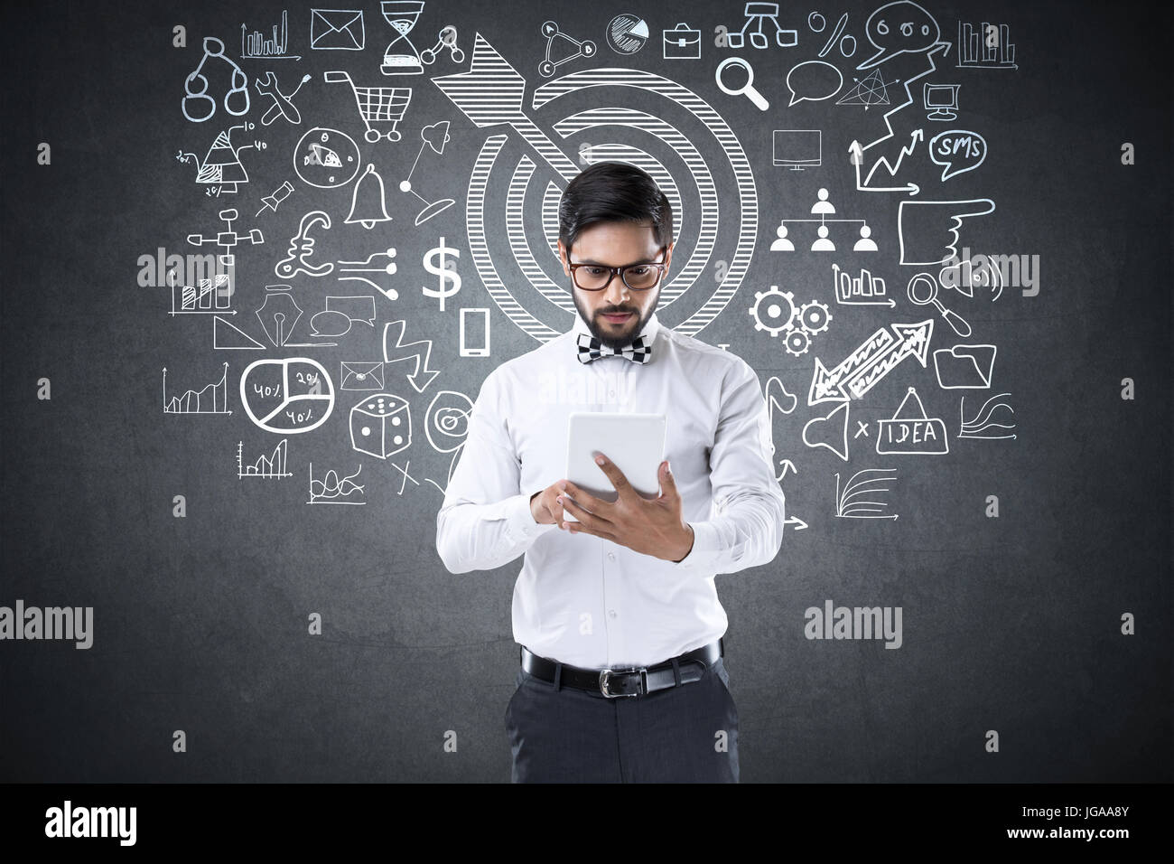 Businessman using digital tablet in front of blackboard avec icônes d'affaires et de technologie Banque D'Images