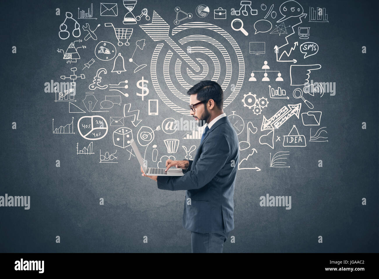 Businessman using laptop in front of blackboard avec icônes d'affaires et de technologie Banque D'Images