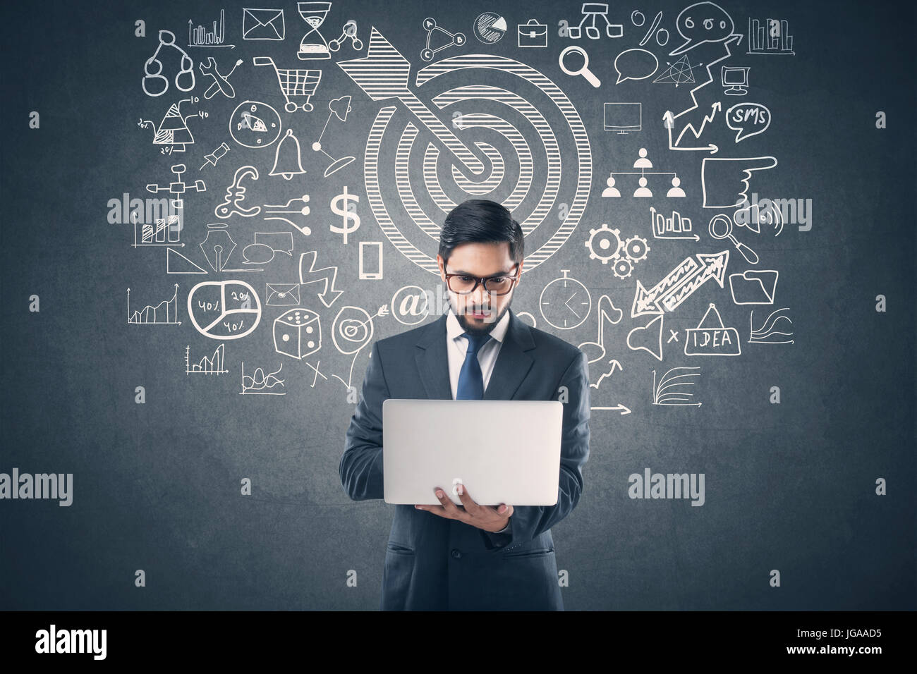 Businessman using laptop in front of blackboard avec icônes d'affaires et de technologie Banque D'Images