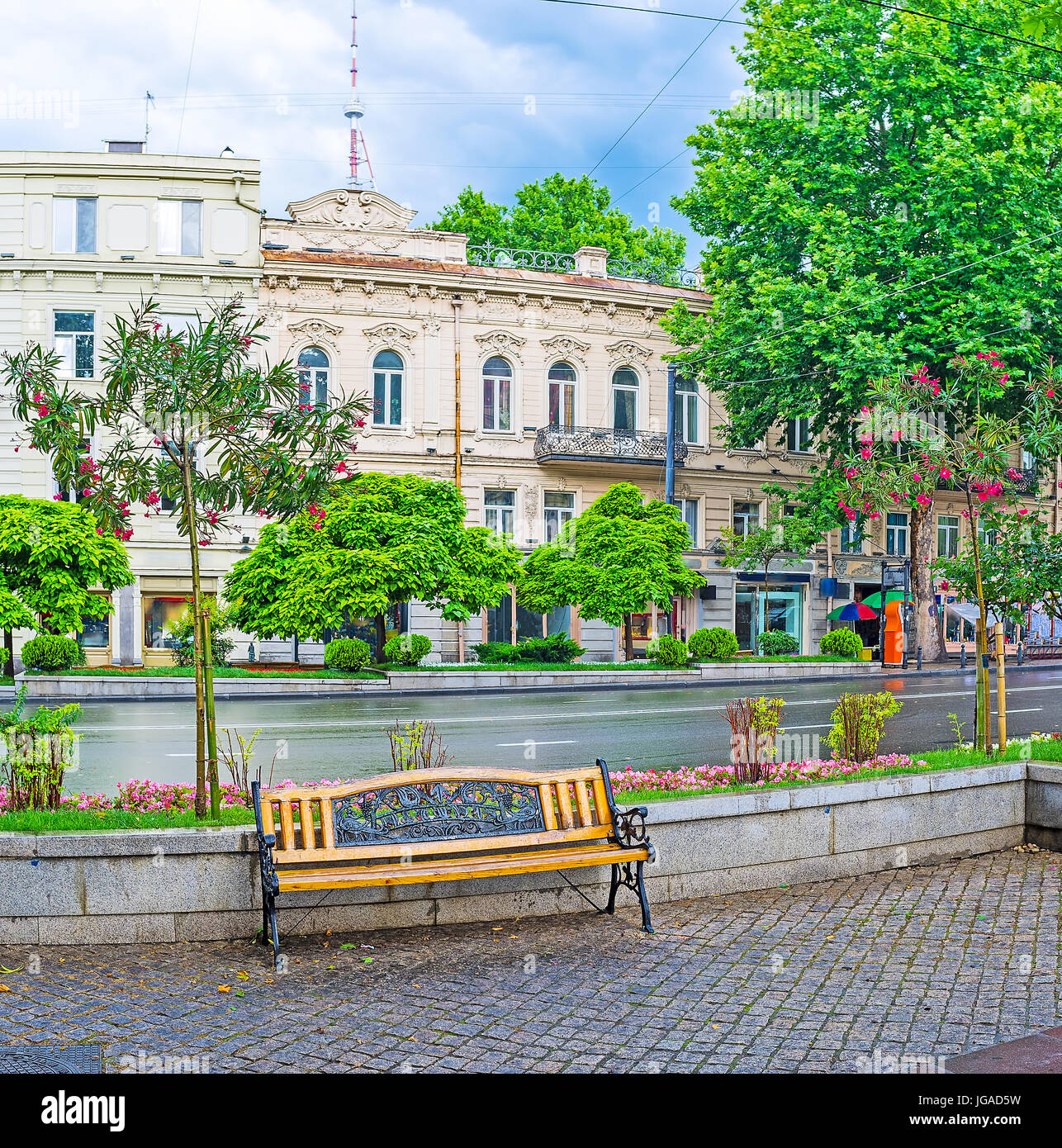 La saison des pluies l'avenue rustaveli avec lonely banc, entouré de massifs de fleurs et arbres en fleurs, avec les édifices historiques sur l'arrière-plan, Tbilissi, Géorgie Banque D'Images