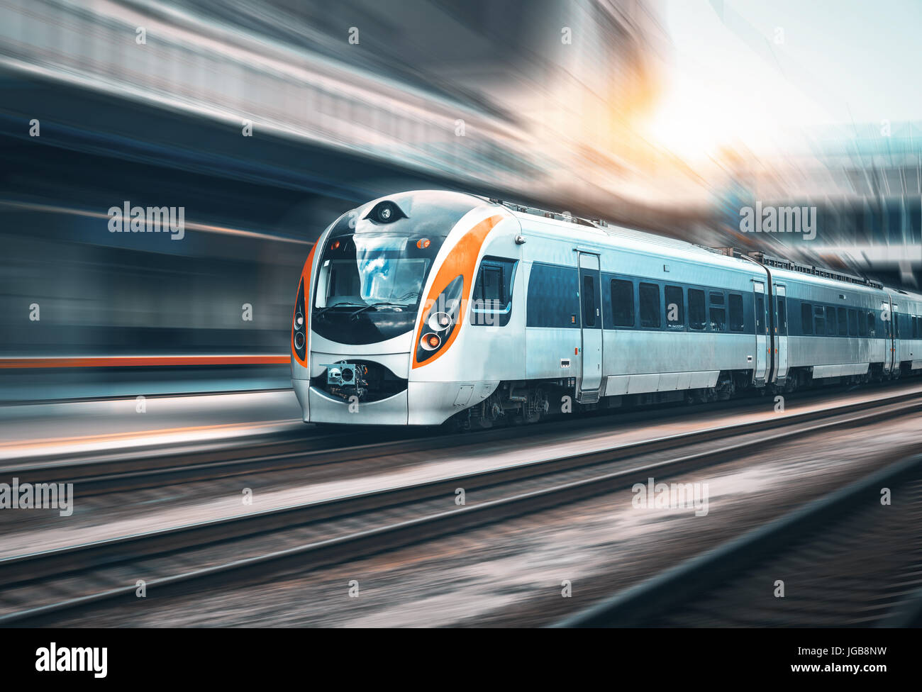 Train à grande vitesse en mouvement à la gare au coucher du soleil en Europe. Train intercity modernes sur la plate-forme ferroviaire avec effet de flou. L'industrie Banque D'Images