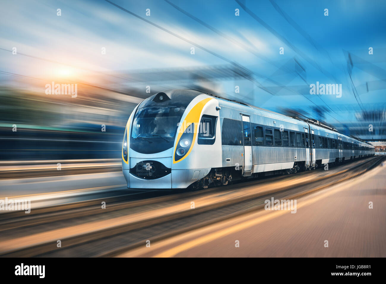 Train à grande vitesse en mouvement à la gare au coucher du soleil en Europe. Train intercity modernes sur la plate-forme ferroviaire avec effet de flou. L'industrie Banque D'Images