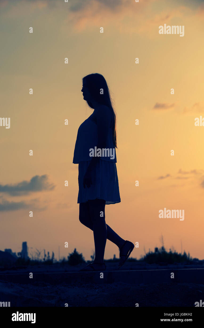 Longueur totale silhouette d'une femme à l'extérieur de marche au coucher du soleil Banque D'Images