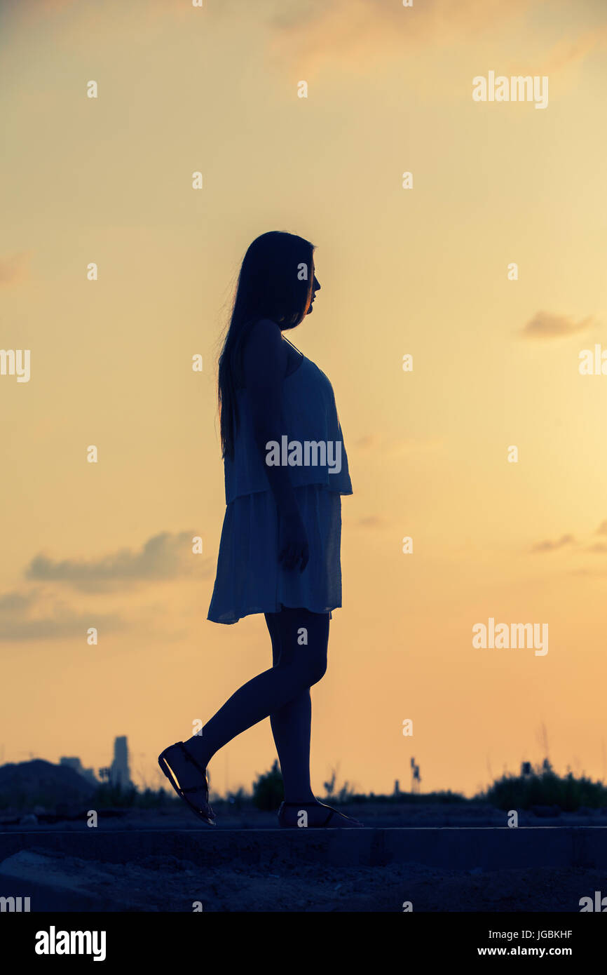 Longueur totale silhouette d'une femme à l'extérieur de marche au coucher du soleil Banque D'Images