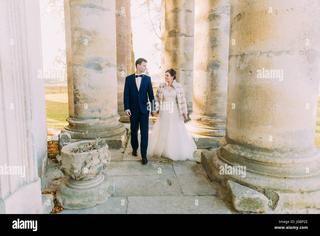 Les nouveaux mariés sont main dans la main tout en marchant entre les colonnes de l'ancienne église. Banque D'Images