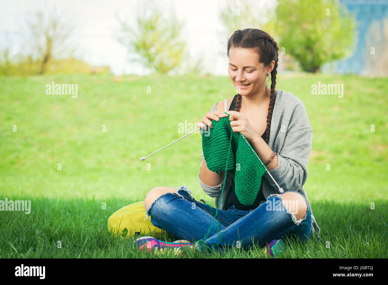 Jeune femme à la mode d'un chandail vert knits knitting sur l'herbe verte un jour d'été Banque D'Images