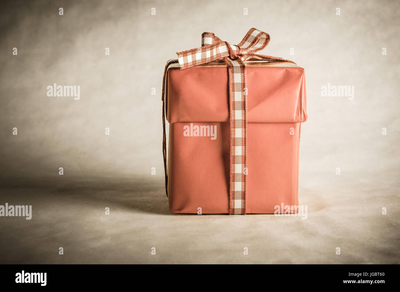 Un solitaire, old vintage styled tourné d'un cadeau de Noël rouge désaturé boîte avec couvercle, attachés avec un arc en ruban vichy (cochée). Banque D'Images