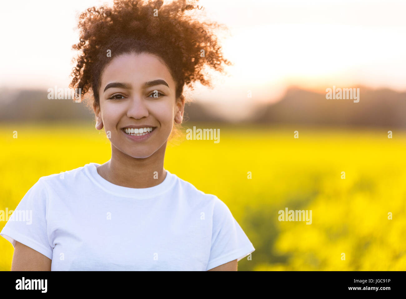 Portrait plein air de belle happy mixed race African American girl adolescent femme jeune femme souriante avec dents parfait dans un champ de fleur jaune Banque D'Images