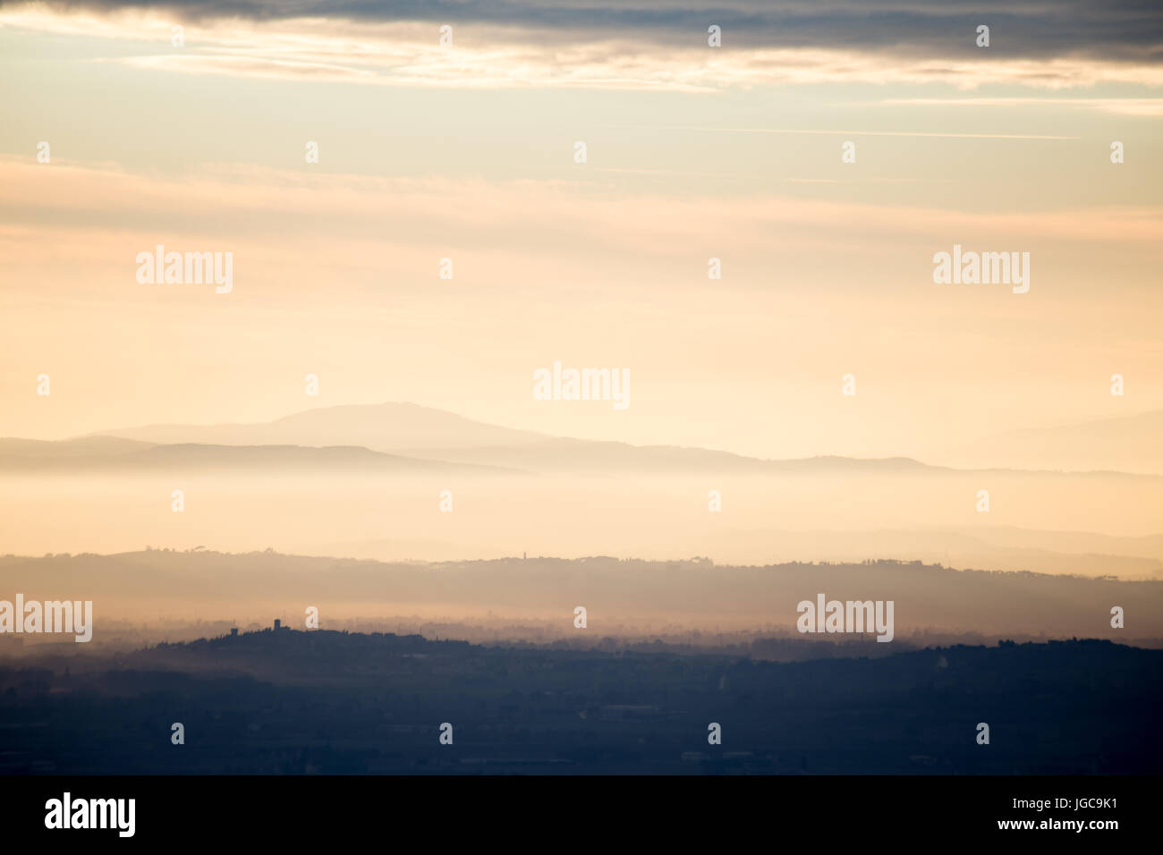 Différentes couches de montagnes et de collines au milieu d'un golden, voyant orange au coucher du soleil, avec des nuages en raison également de la lumière, et les villes skylines Banque D'Images