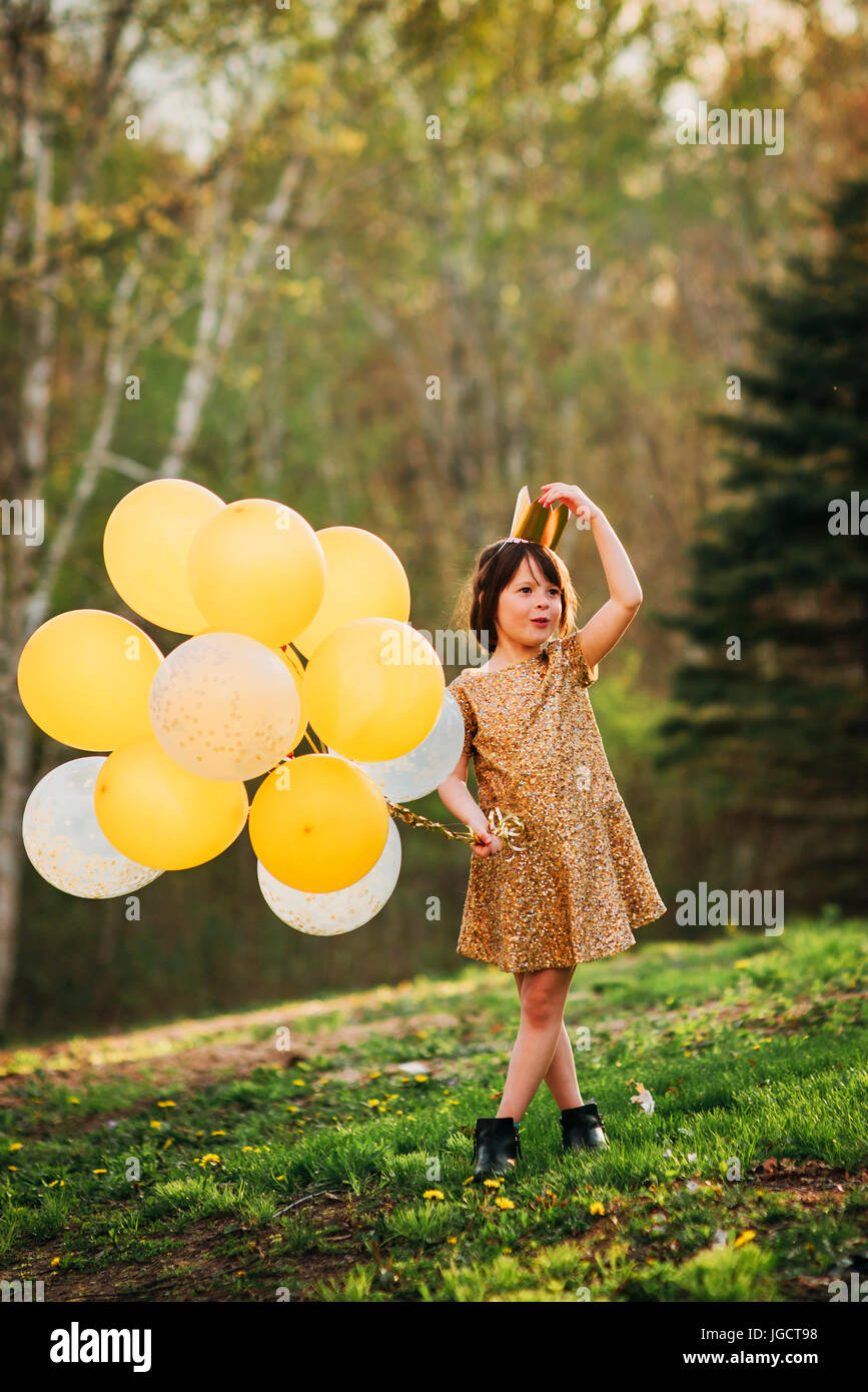 Jeune fille dans une robe d'or portant une couronne portant des ballons Banque D'Images