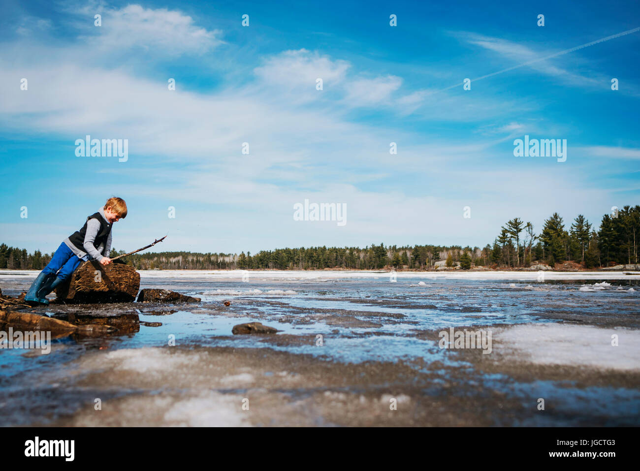 Garçon debout par un lac gelé tenant un bâton Banque D'Images