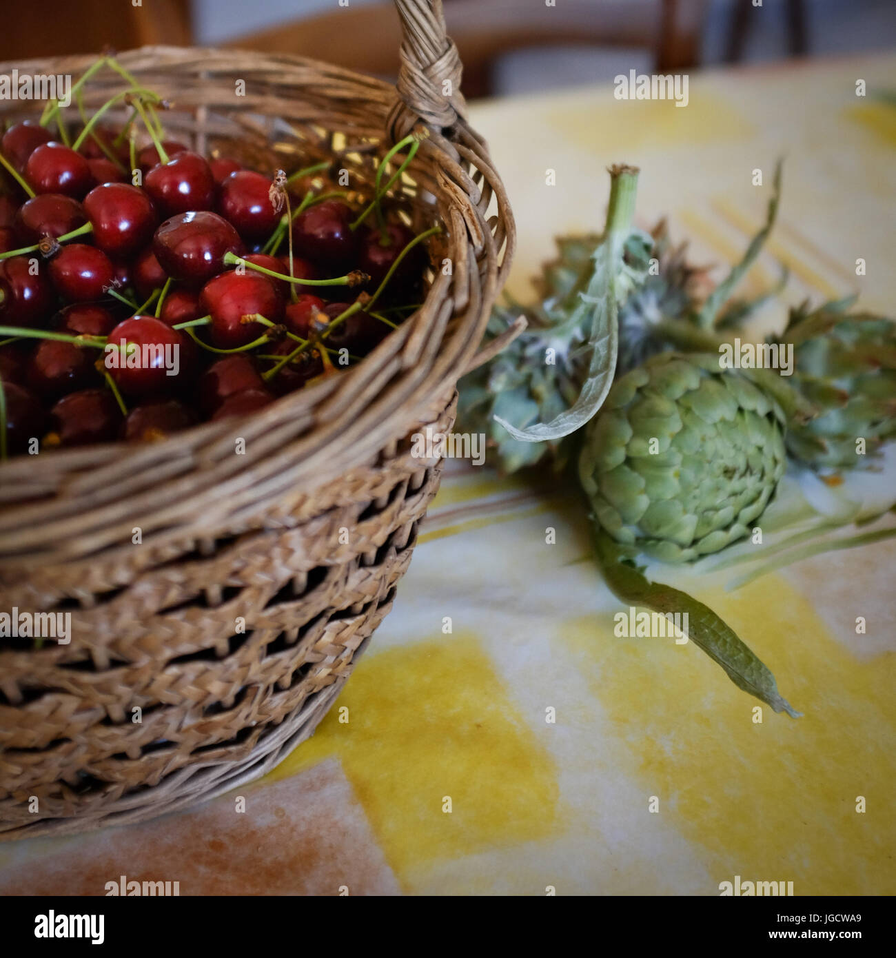 Panier en osier avec cerises et artichauts Banque D'Images