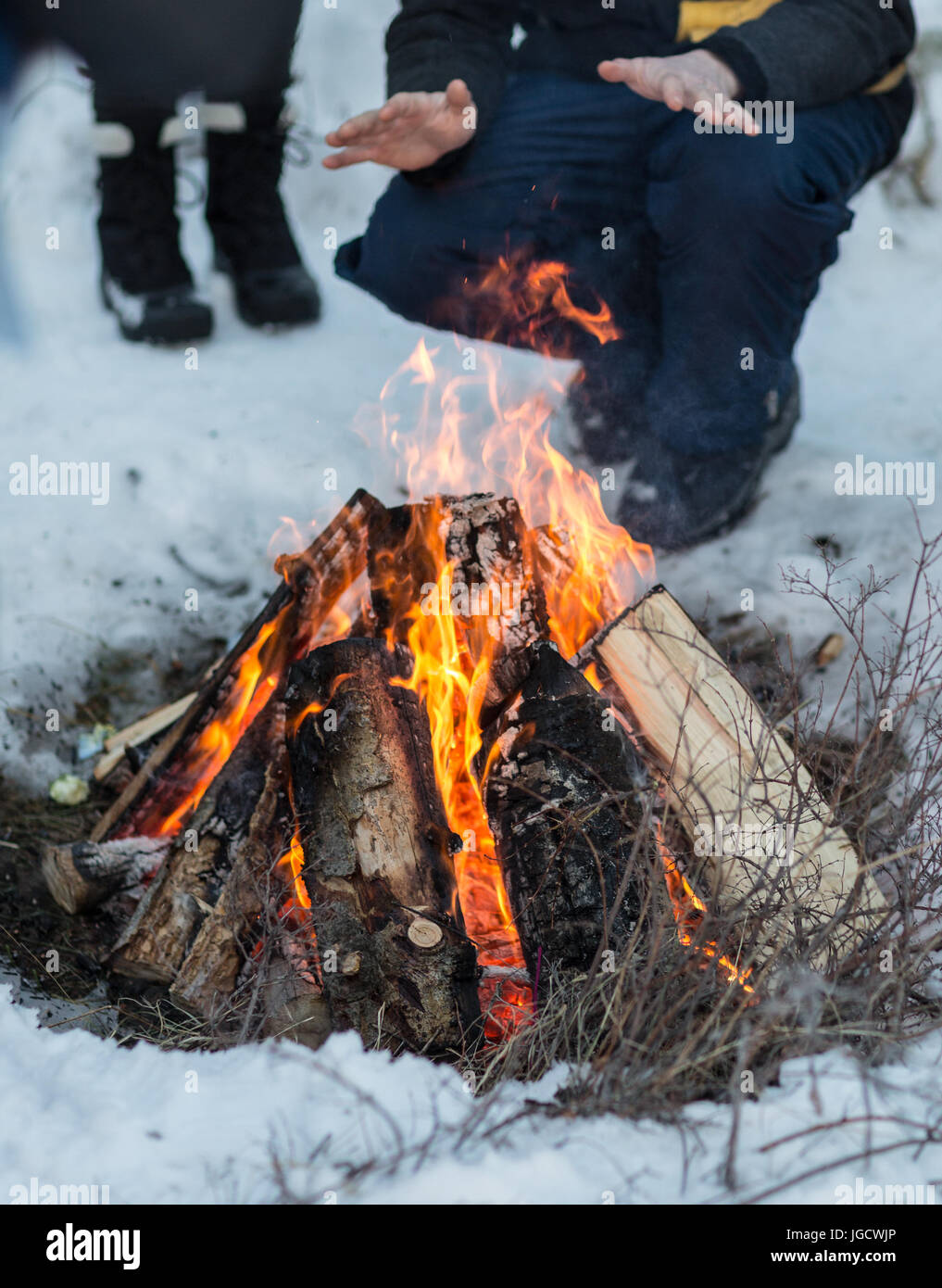 L'homme accroupi près d'un feu de camp dans la neige ses mains réchauffement Banque D'Images