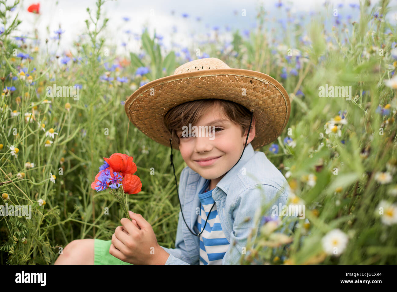 Smiling boy assis dans un champ de fleurs sauvages tenant un bouquet de fleurs Banque D'Images