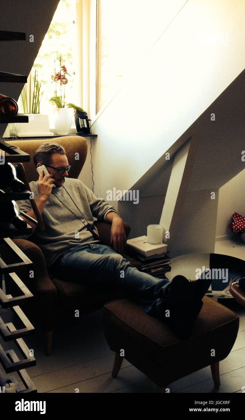 Man relaxing in chair talking on a mobile phone Banque D'Images