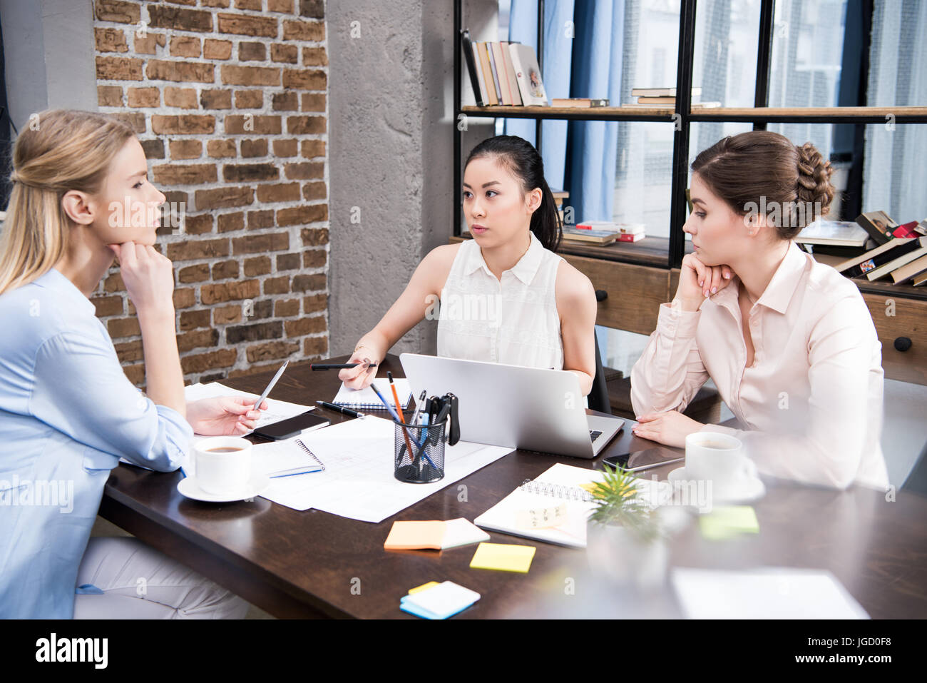 Pensive multicultural businesswomen discussing projet d'entreprise sur le lieu de travail avec ordinateur portable Banque D'Images