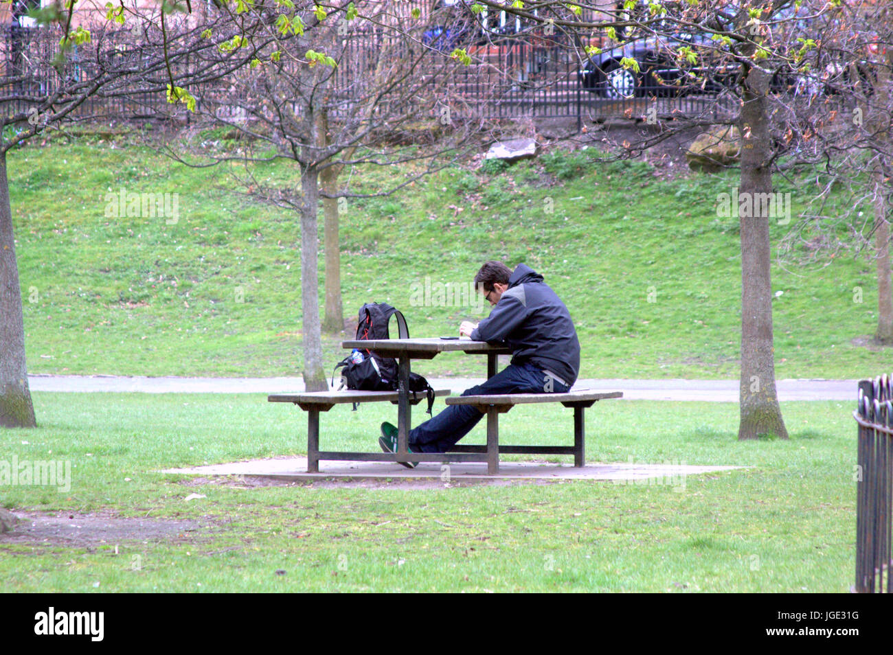 Jeune homme étudiant adolescent assis seul dans la contemplation à table de pique-nique banc dans un parc public avec sac à dos pour entreprise Banque D'Images