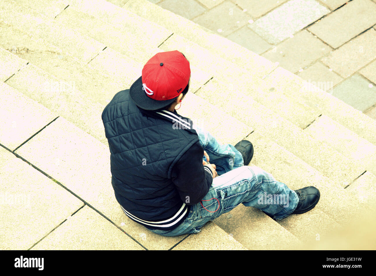 Jeune homme étudiant adolescent assis seul dans la contemplation d'oursons rouge hat trendy vêtements de mode scène coloré Banque D'Images