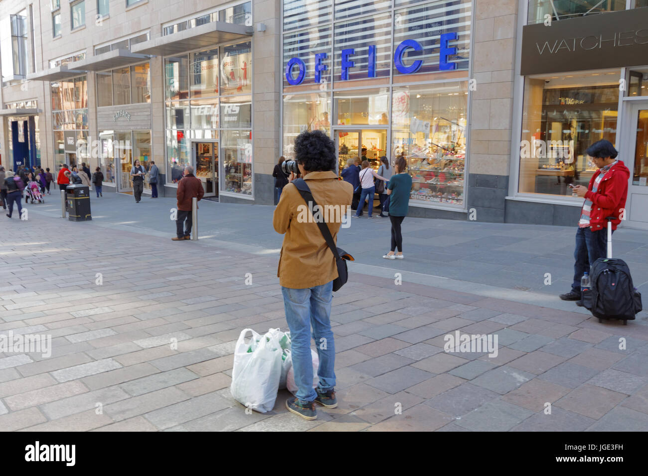 Jeune homme à la mode adolescent étudiant à prendre des photos avec l'appareil photo de la rue de Glasgow Buchanan Street photographe amateur de shopping with shopping bags Banque D'Images