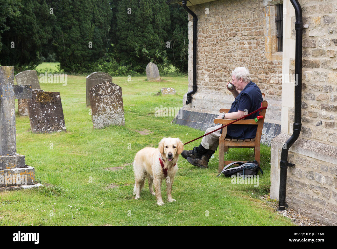 Dog walker - un homme s'asseoir pour se reposer dans un cimetière, tandis que la promenade du chien, Appleton, Oxfordshire UK Banque D'Images