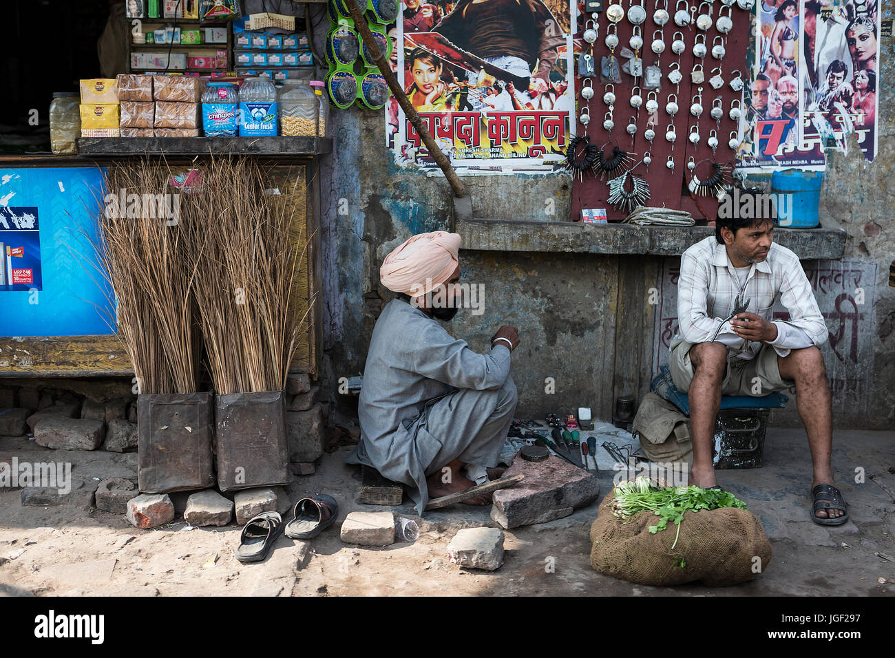 Deux serruriers Indiens attendent assis au bord de la route avec leurs outils pour tailler des clés et une sélection de cadenas, près d'une rangée de boutiques Banque D'Images