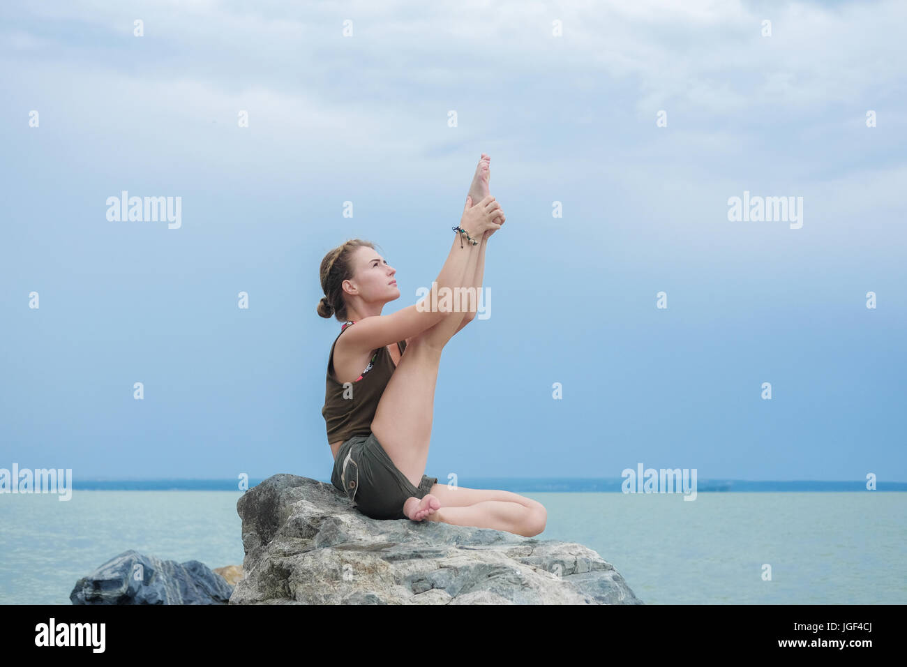 Girl practicing yoga on the rocks contre le ciel bleu et la mer d'azur. Relaxation et étirement. Jeune femme sportive slim faire du yoga à l'extérieur. Banque D'Images