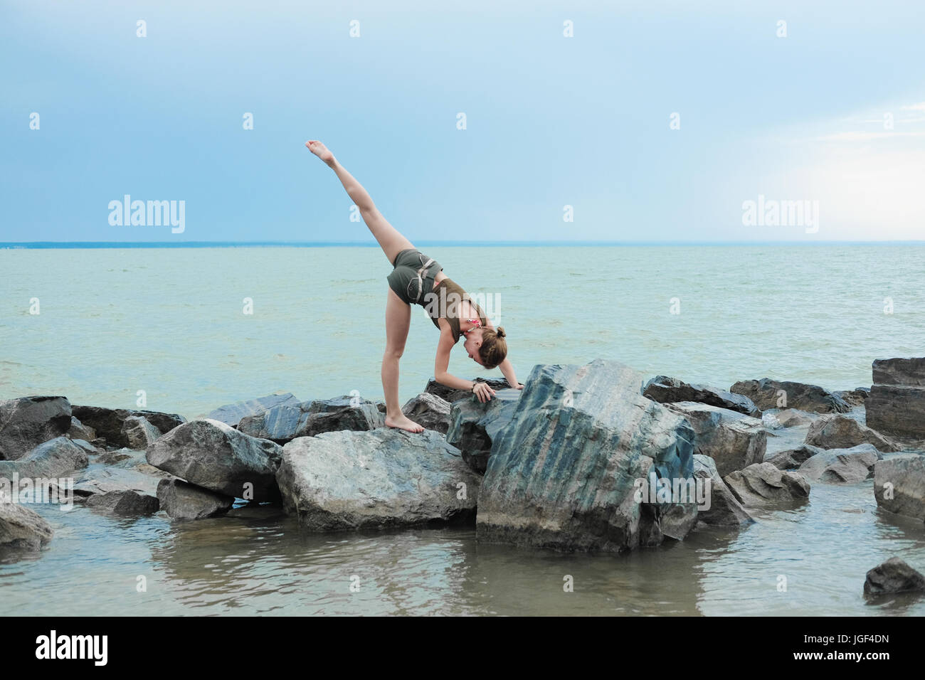 Girl practicing yoga on the rocks contre le ciel bleu et la mer d'azur. Relaxation et étirement. Jeune femme sportive slim faire du yoga à l'extérieur. Banque D'Images