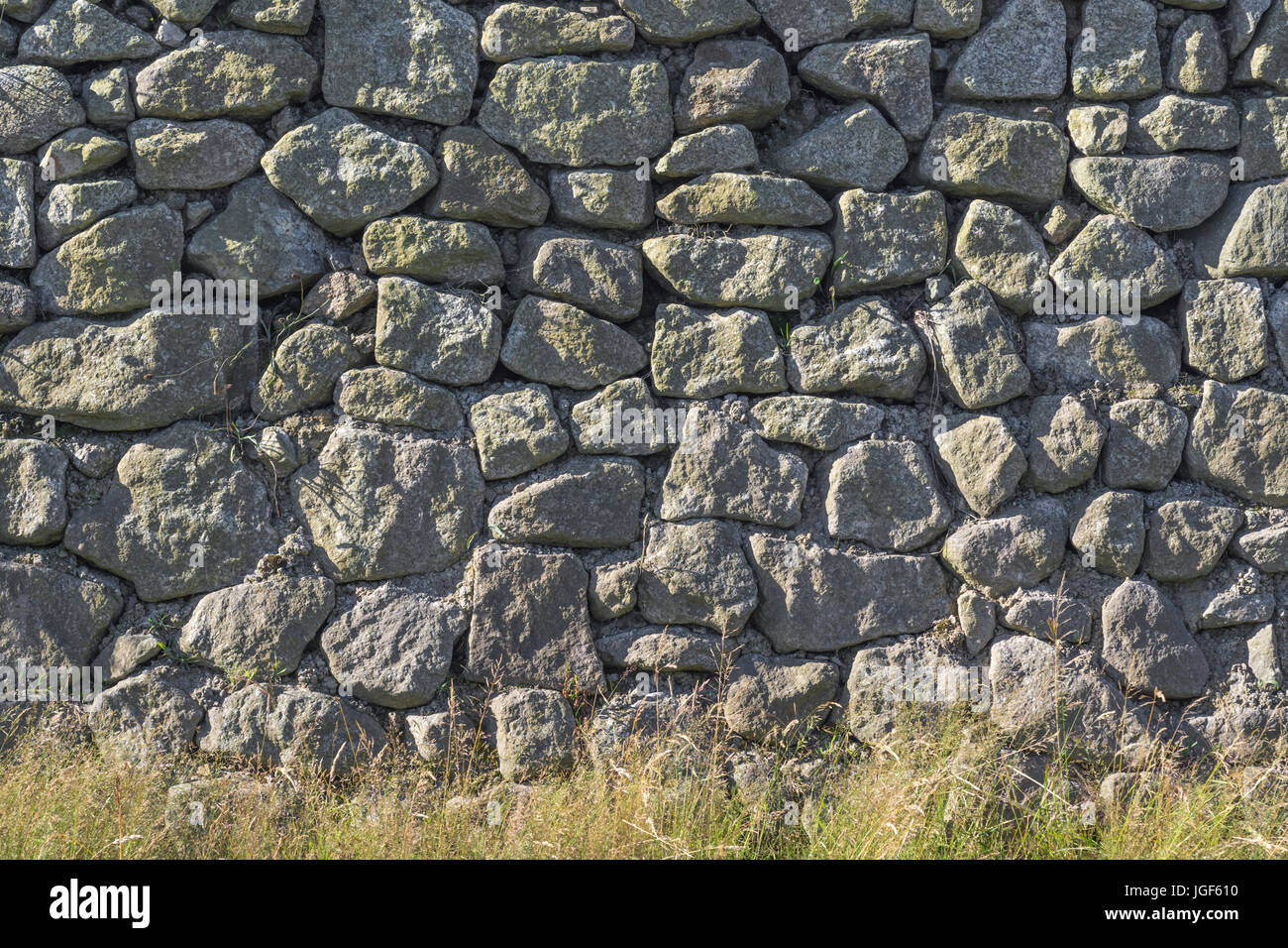 Travaux de maçonnerie irréguliers / mur en pierre de granit de bord de route avec végétation de bordure d'herbe. Banque D'Images