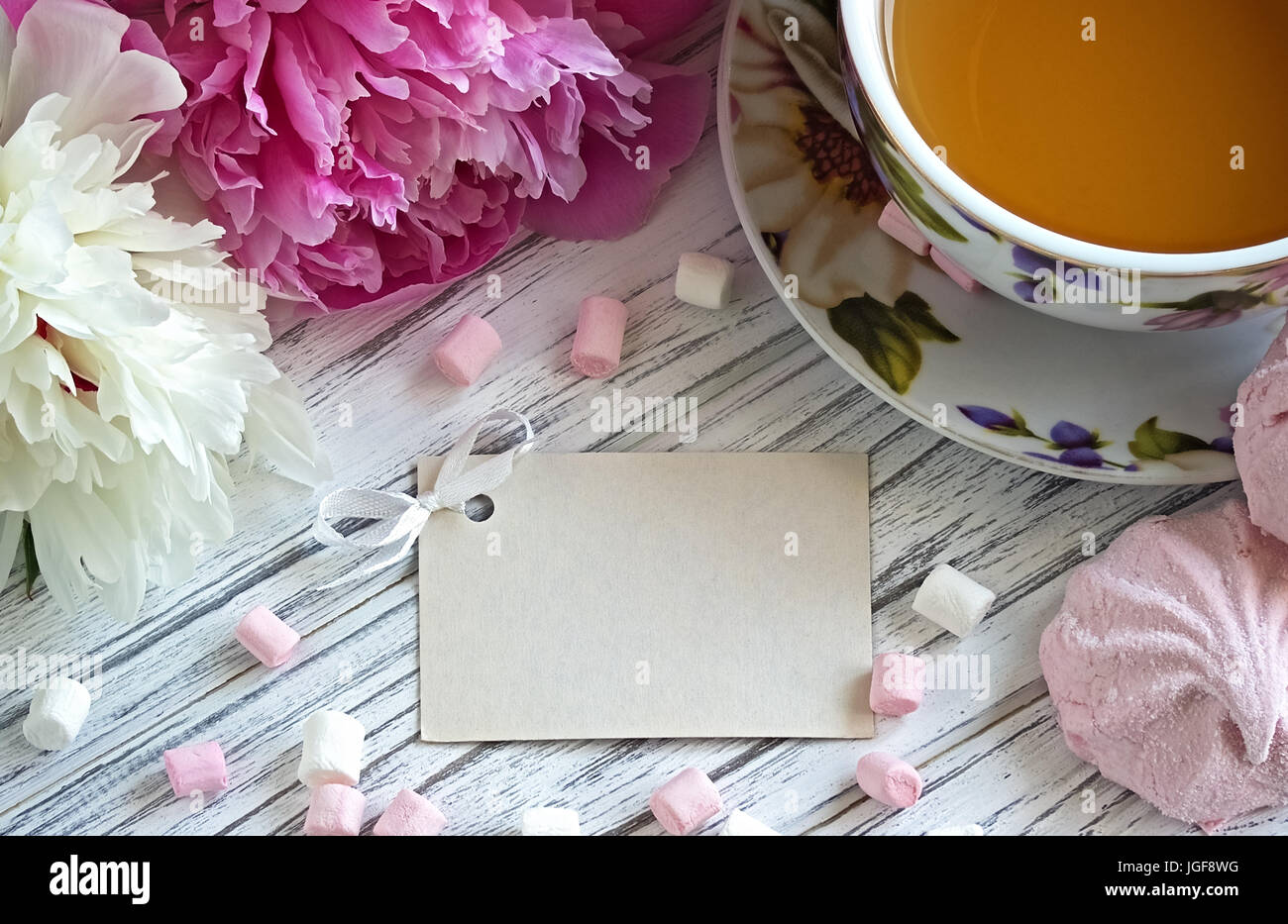 Les Pivoines rose fleurs tasse de thé carte de souhaits marshmallow sur un fond en bois blanc - stock image Banque D'Images