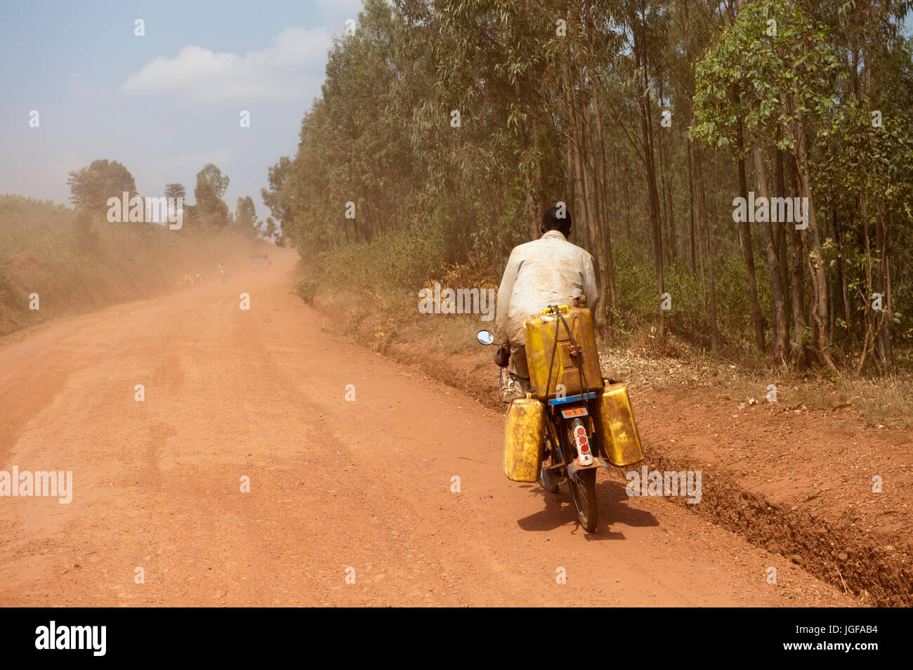 L'homme sur une moto transportant des conteneurs d'eau le long d'une route poussiéreuse, le Rwanda. Banque D'Images