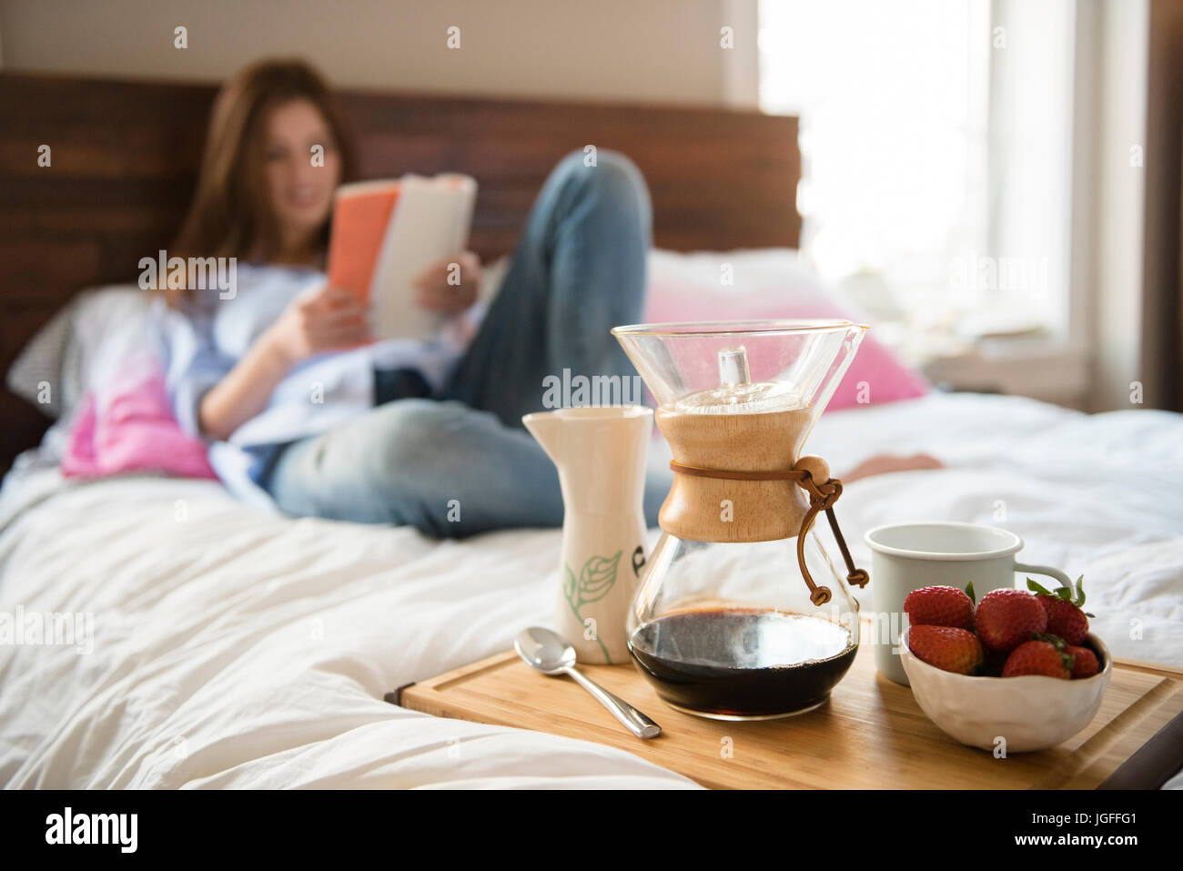 Caucasian woman laying in bed reading book près de plateau du petit déjeuner Banque D'Images