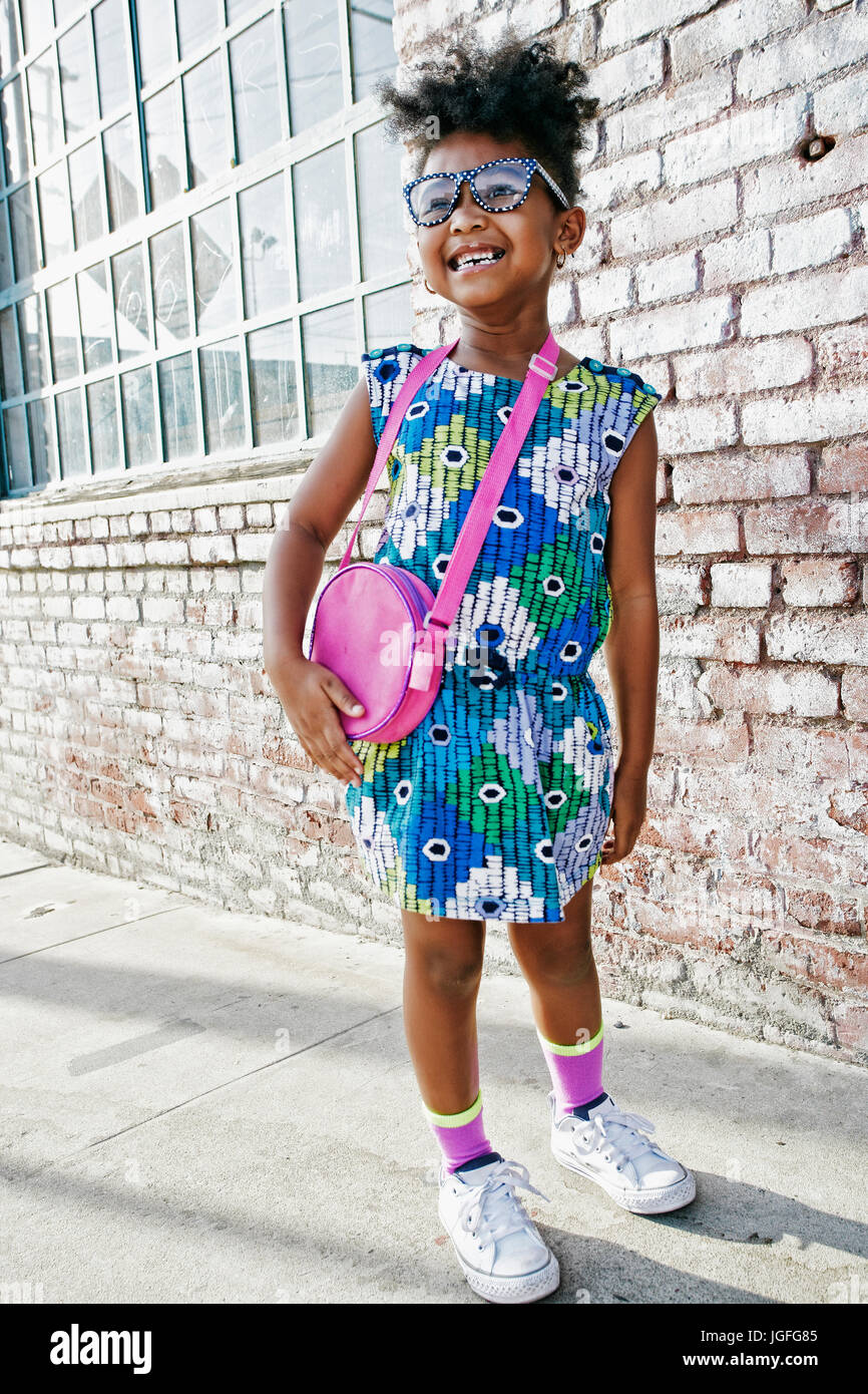 Smiling Black Girl standing on sidewalk portant robe et sac à main Banque D'Images