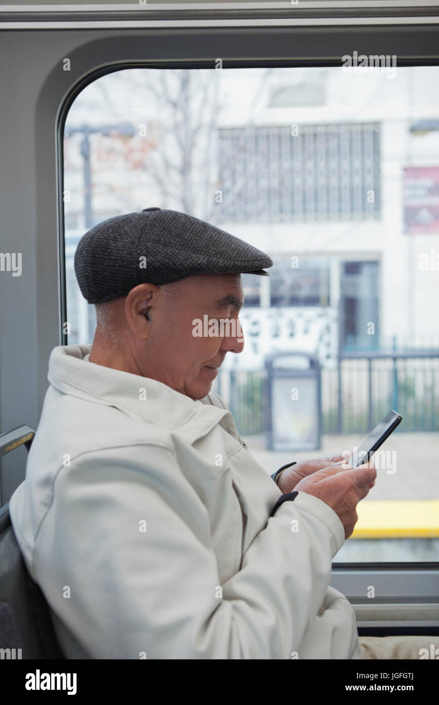 Hispanic man sitting on train texting on cell phone Banque D'Images