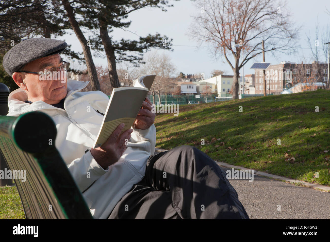 Hispanic man sitting on park bench reading book Banque D'Images