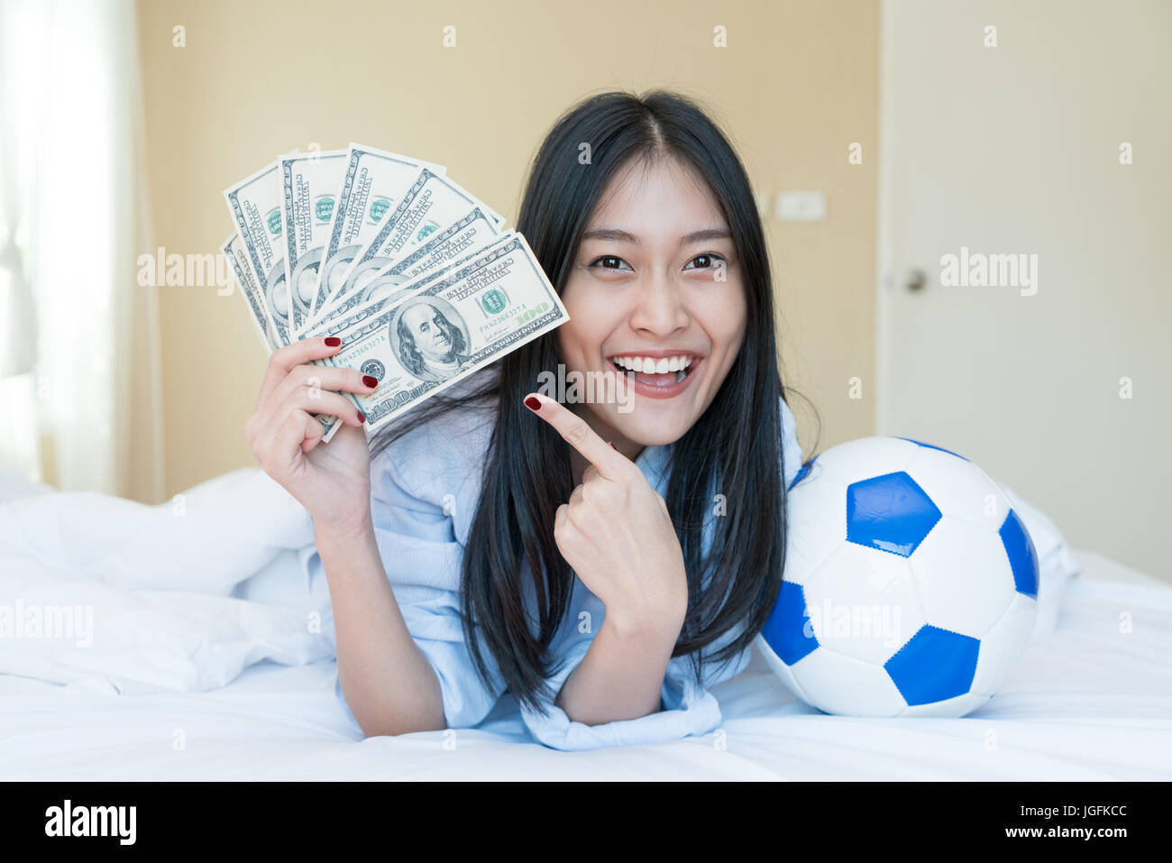 Le football et l'argent. Young Asian woman holding soccer ball et de l'argent dans la chambre à la maison. Jeu de loterie concours idée concept Banque D'Images