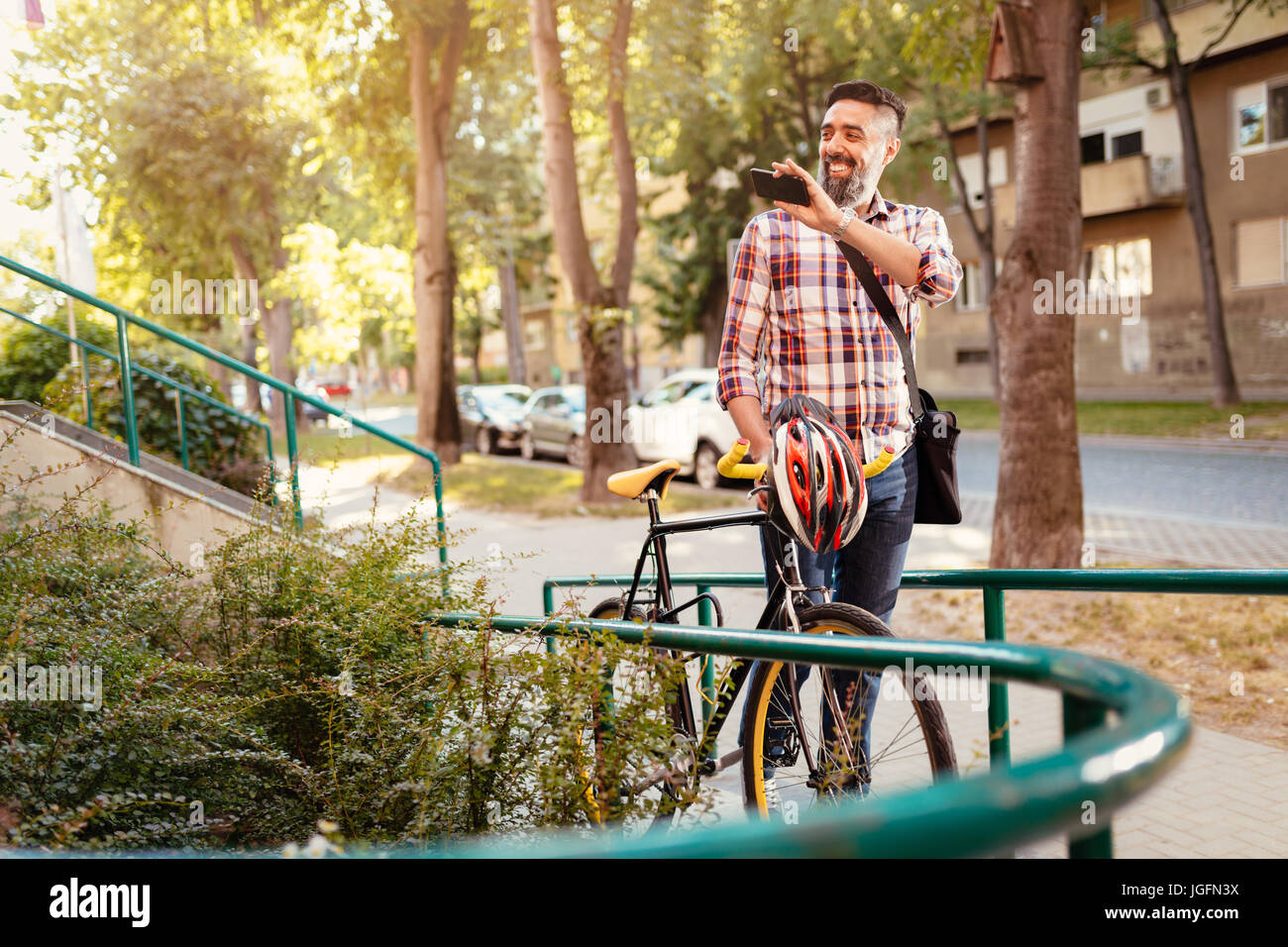 Businessman aller au travail en vélo. Il marche à côté du vélo, holding smartphone et forme Bonjour. Banque D'Images