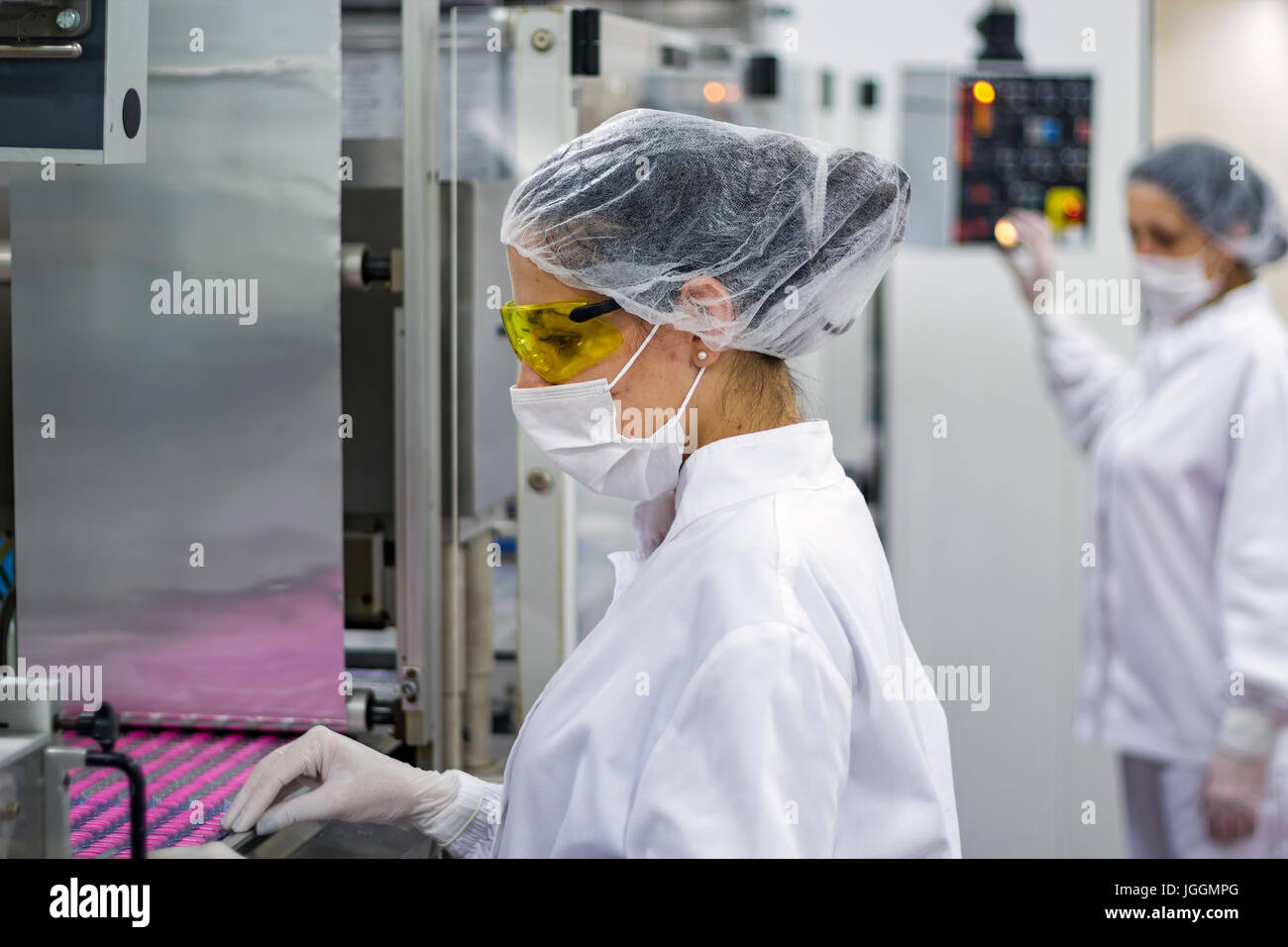 Travailleurs pharmaceutiques maîtriser l'emballage des comprimés médicaux. Technolgists pharmaceutique le port de vêtements protecteurs. Banque D'Images