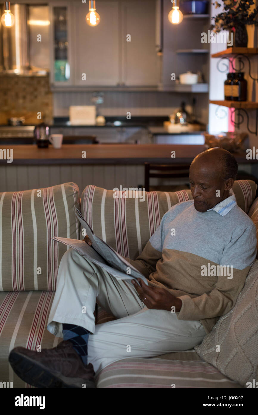 Man reading newspaper while sitting on sofa in living room à la maison Banque D'Images