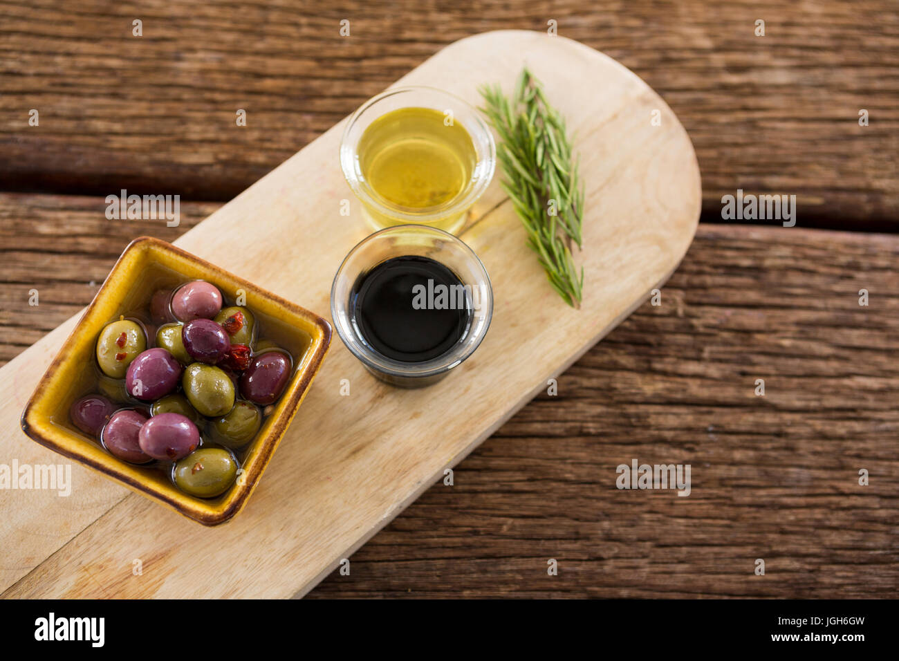 Close-up of olive mariné, le romarin avec de l'huile d'olive et de vinaigre balsamique sur plateau en bois Banque D'Images