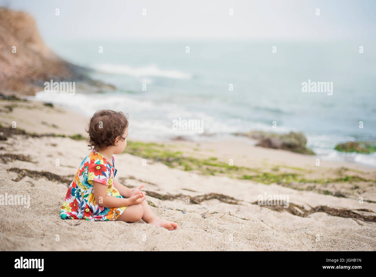 Petite fille en robe colorée de fleurs assis tout seul la mer Banque D'Images