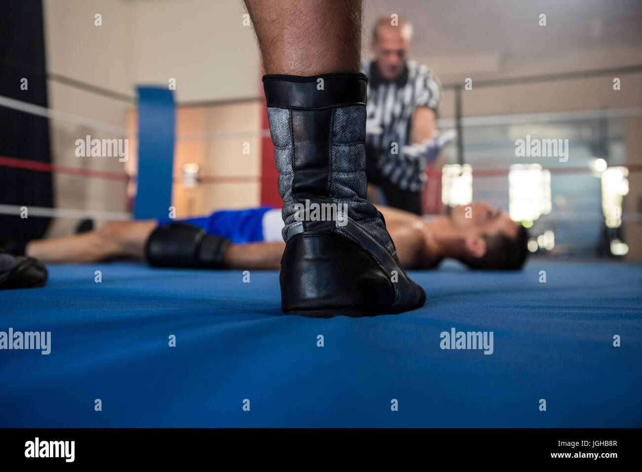 La section basse de male boxer debout contre l'arbitre par athlète couché dans ring de boxe Banque D'Images