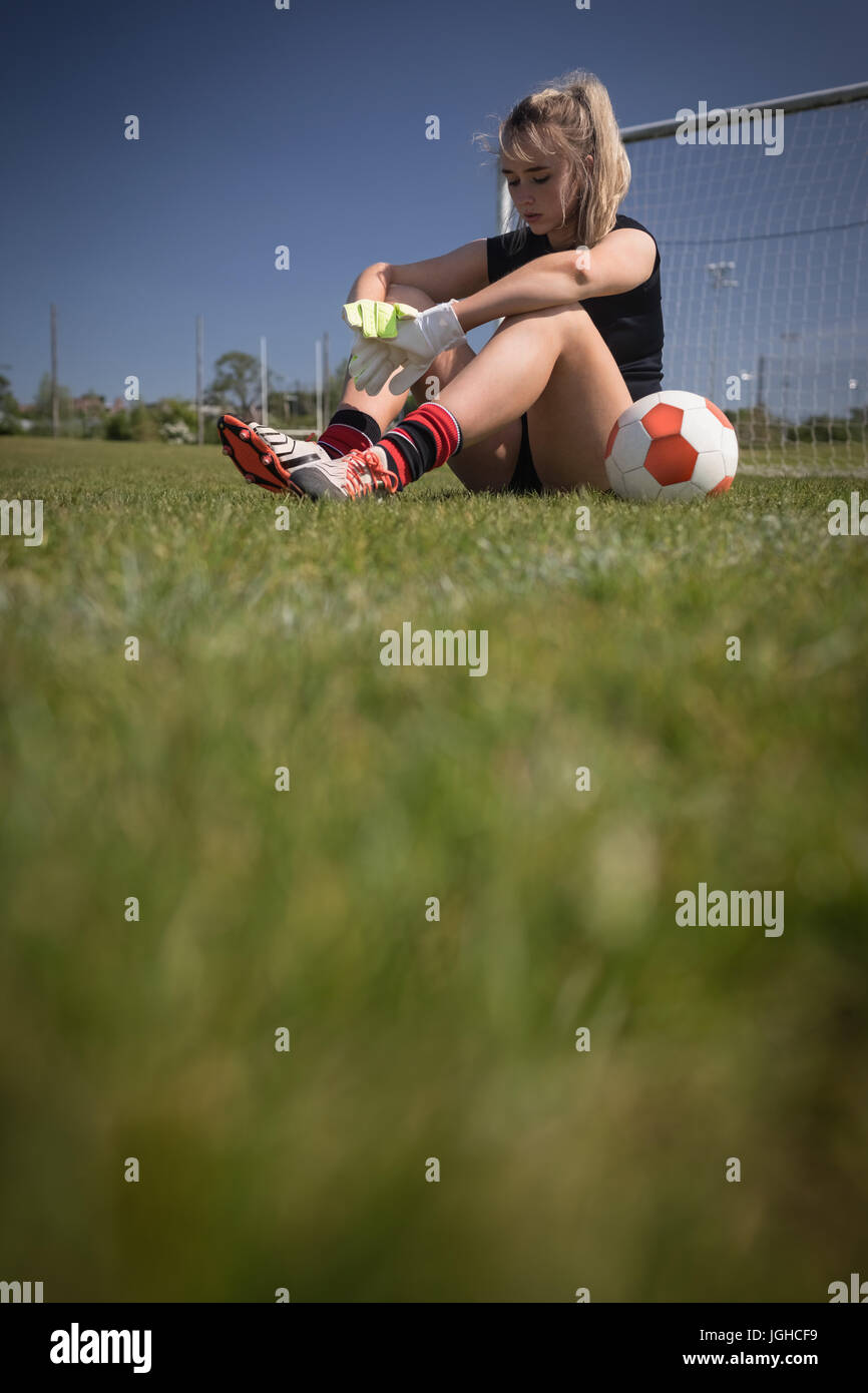 Toute la longueur du joueur de soccer féminin fatigué assis par poteau de but sur terrain Banque D'Images
