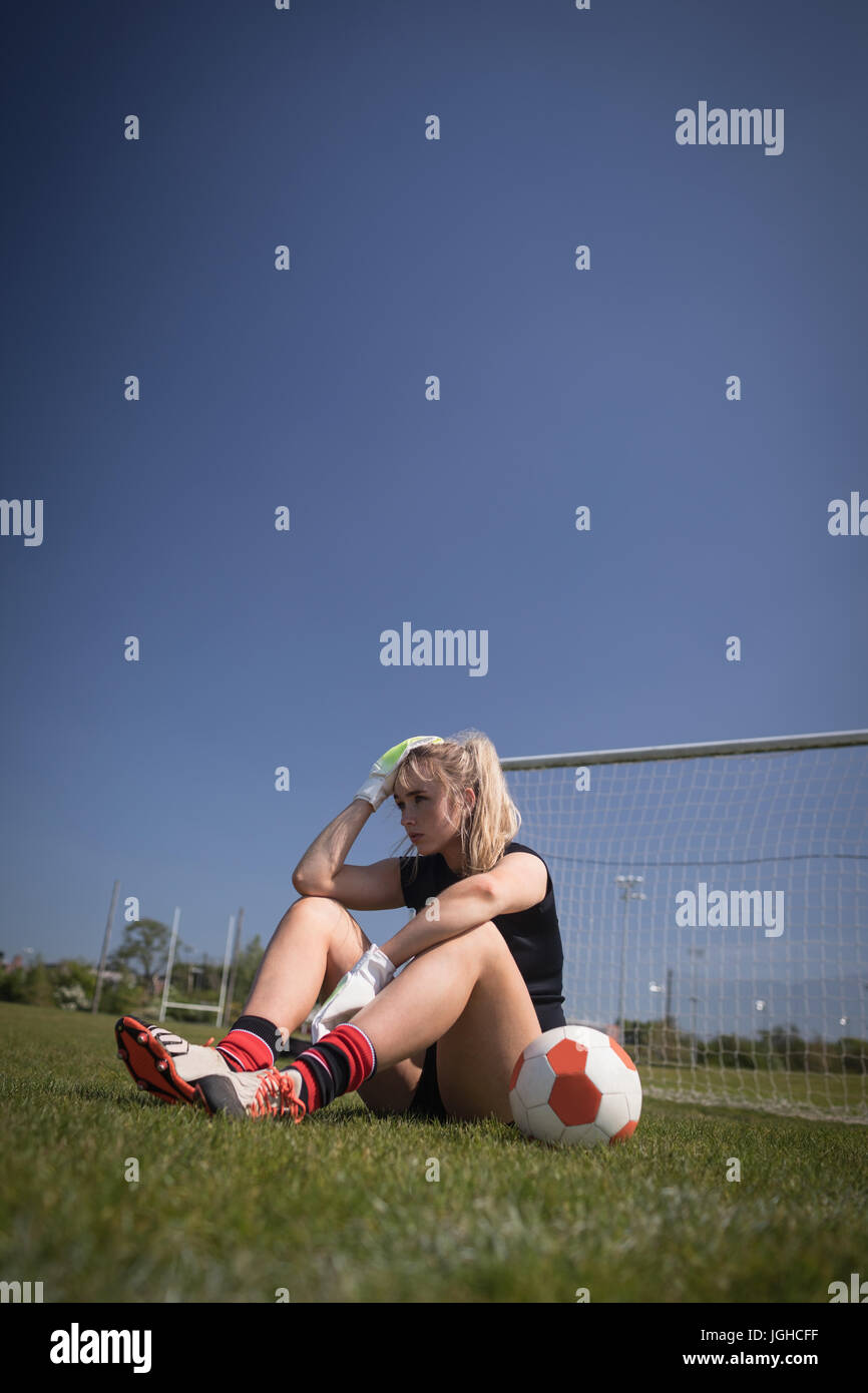 Toute la longueur du joueur de soccer féminin détente sur terrain contre ciel bleu clair Banque D'Images