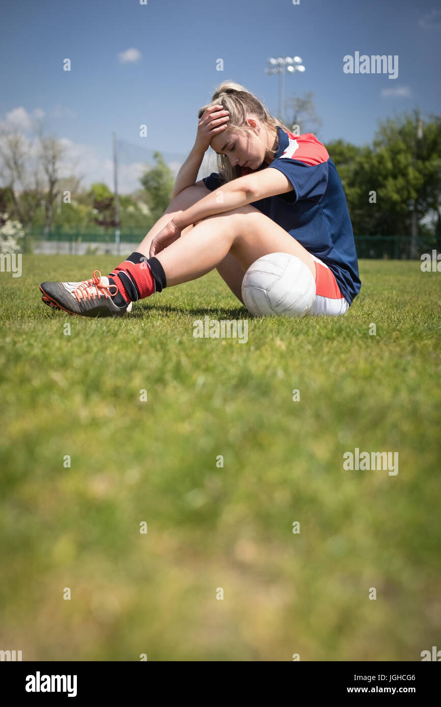 Toute la longueur du joueur de soccer féminin frustré assis sur le terrain au cours de journée ensoleillée Banque D'Images
