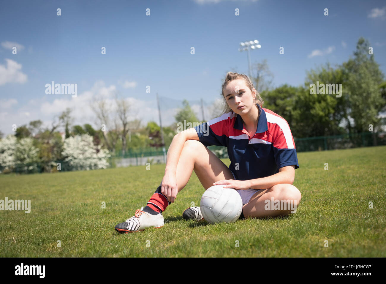 Portrait de jeune femme avec ballon de soccer assis sur terrain against sky Banque D'Images