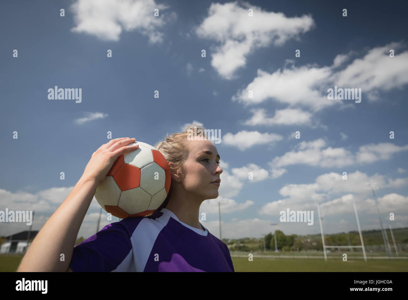 Thoughtful woman holding soccer ball on field against cloudy sky Banque D'Images