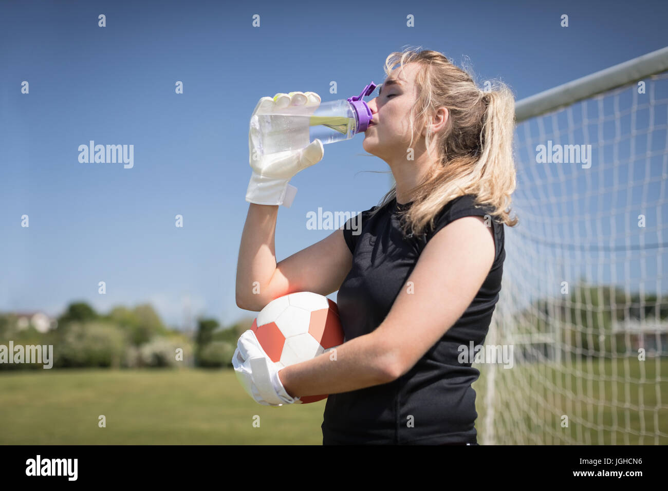 Le joueur de soccer féminin assoiffé d'eau potable sur terrain au cours de journée ensoleillée Banque D'Images