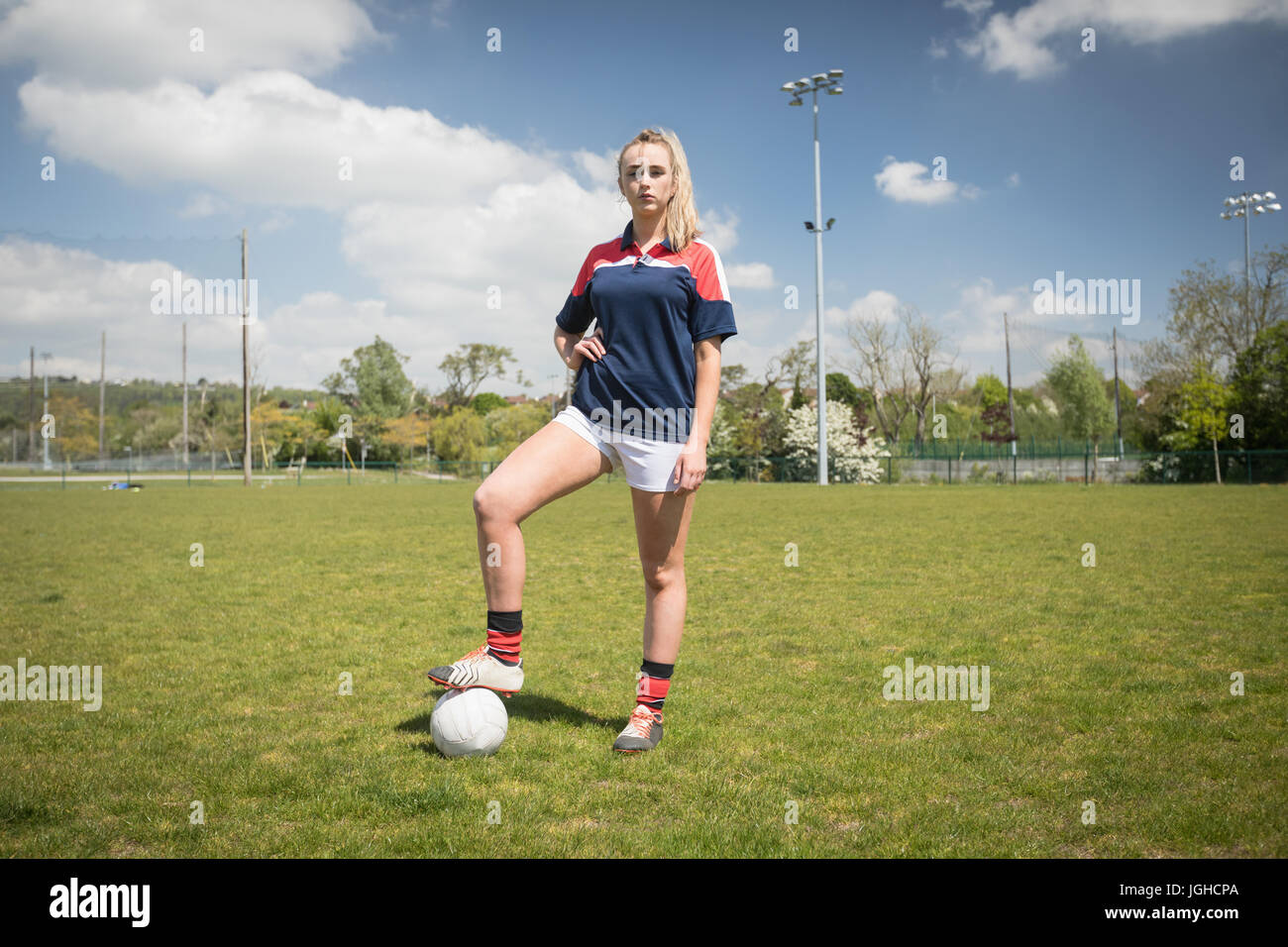 Toute la longueur du joueur avec ballon de soccer féminin sur terrain permanent contre le ciel Banque D'Images
