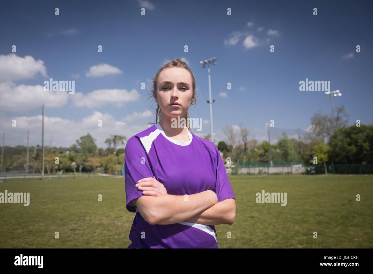 Portrait of female soccer player with arms crossed standing sur terrain against sky Banque D'Images