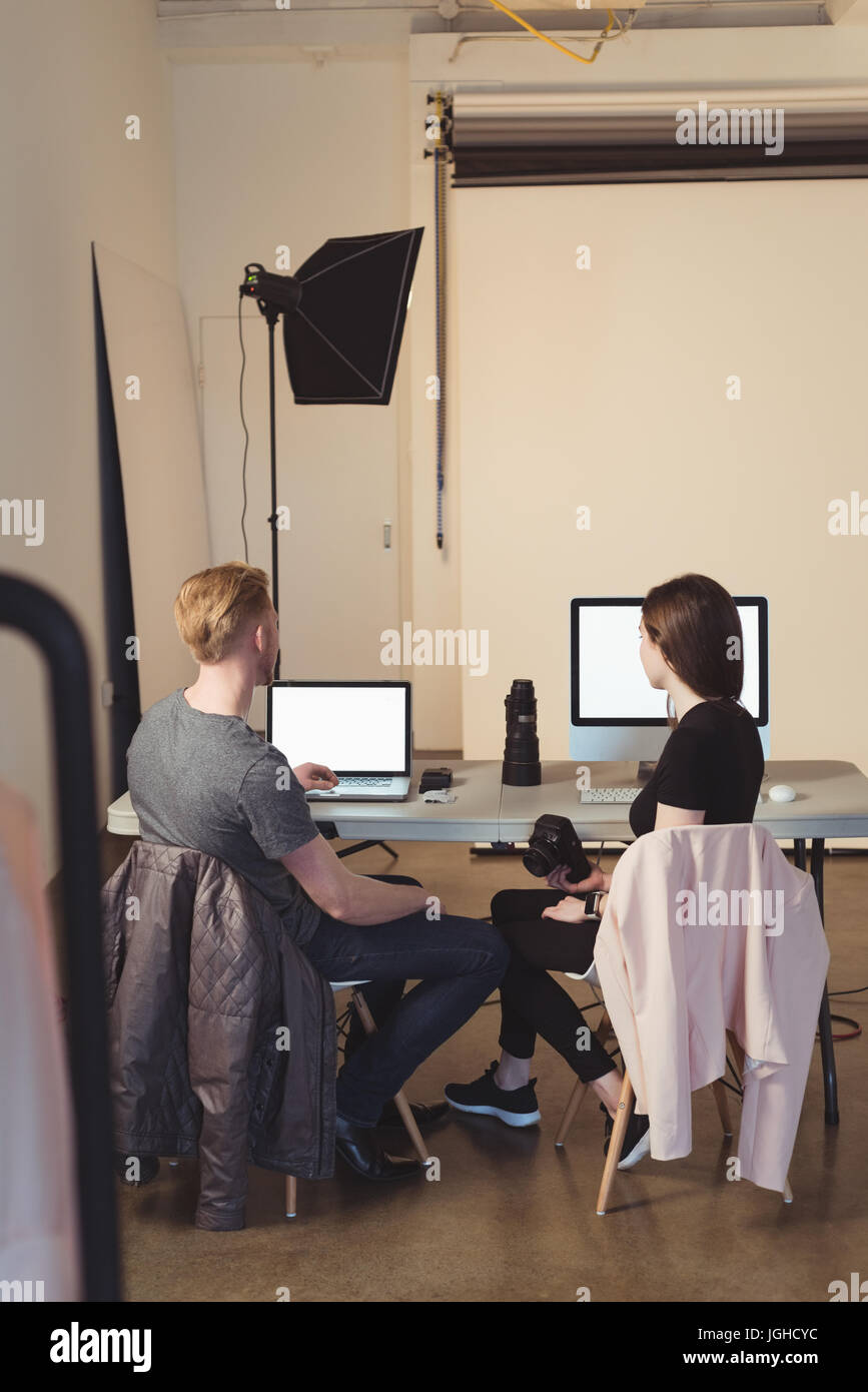 Avec l'aide d'assistant photographe laptop while sitting on chair au studio Banque D'Images